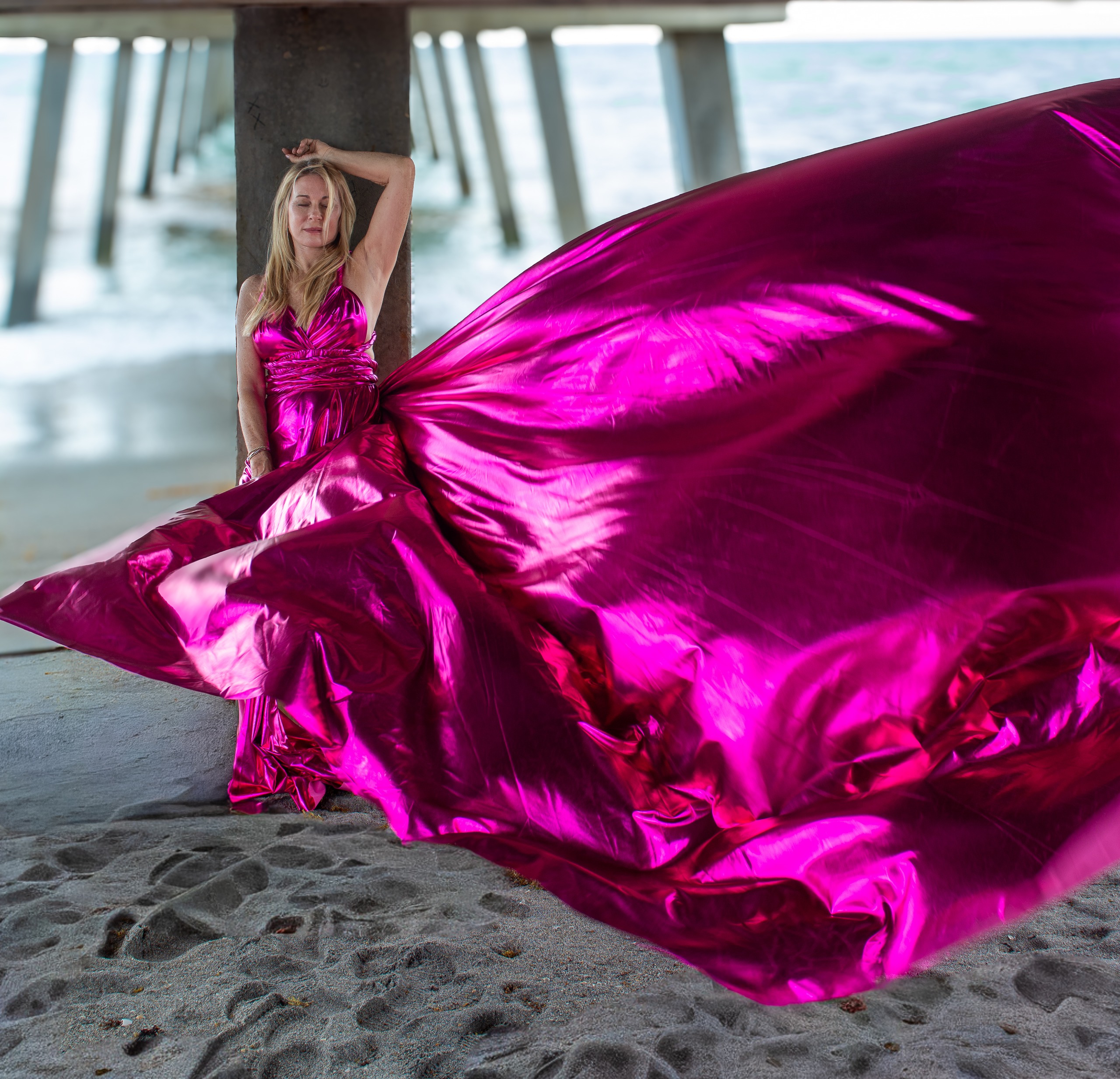 Flying dress photoshoot under the pier — magenta gown billowing
