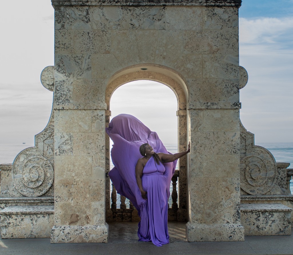 Flying dress photoshoot in a stone archway — purple gown billowing over the ocean
