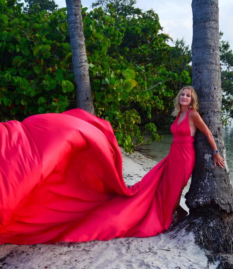 Flying dress photoshoot on the beach — red gown flowing beside a palm tree